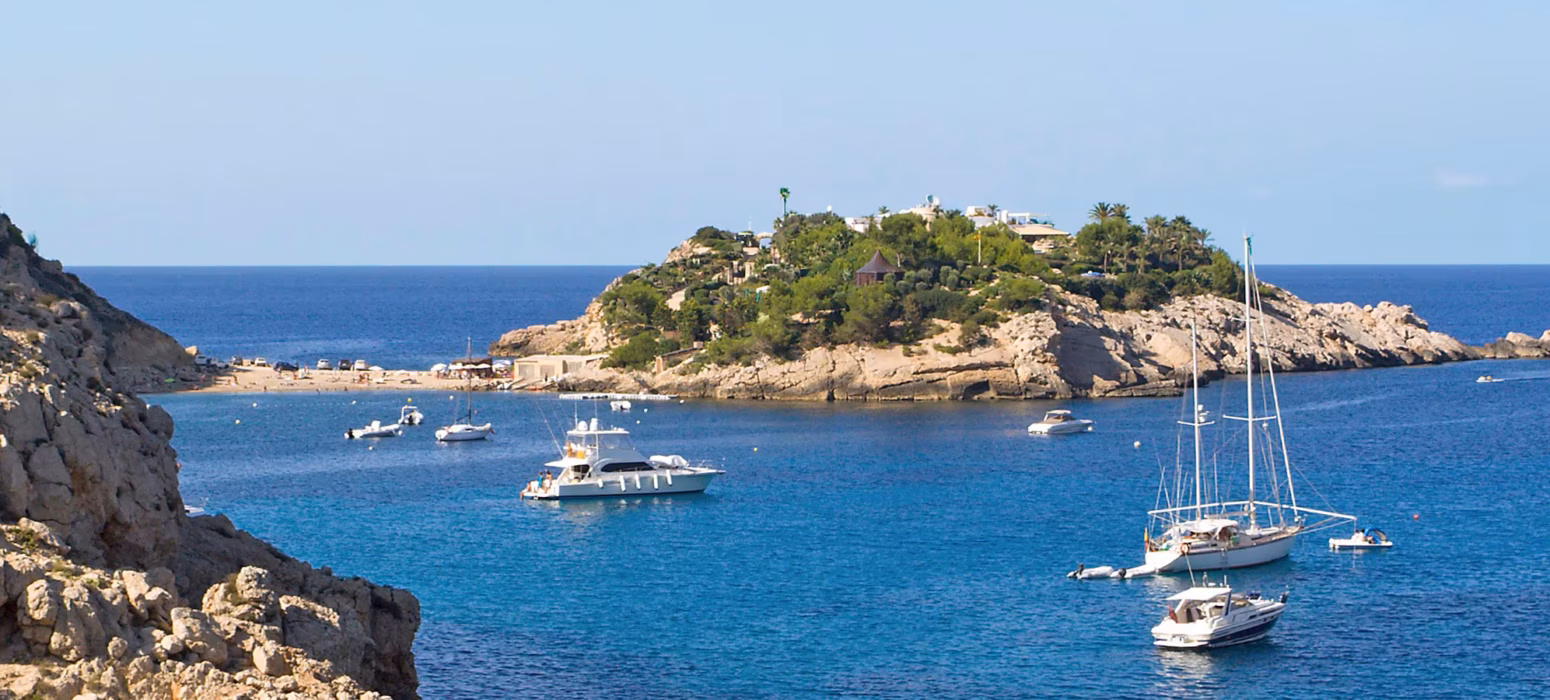 Montagna che scende nel mare con isola e barche ormeggiate nel Mediterraneo